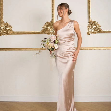 Woman in a long, elegant dress holding flowers in a room with ornate gold frames.
