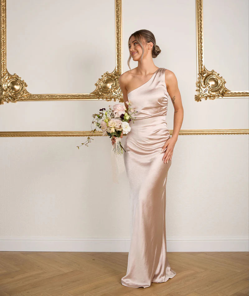 Woman in a long, elegant dress holding flowers in a room with ornate gold frames.
