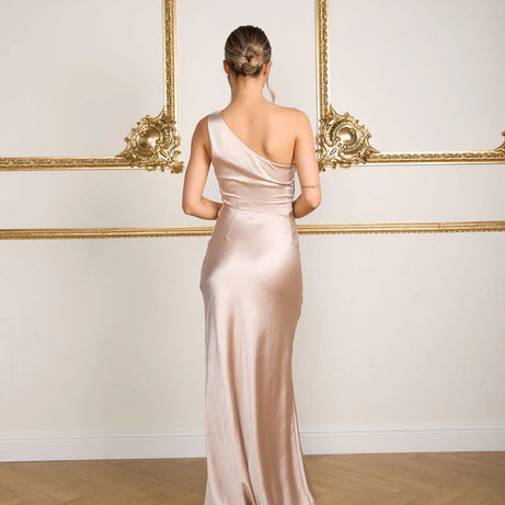 Woman in a one-shoulder bridesmaid dress standing in front of ornate wall decorations.