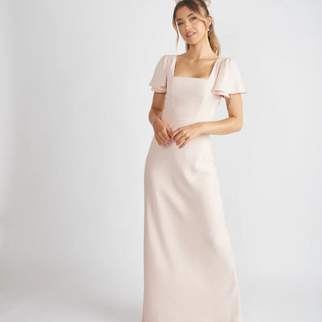Lady wearing light blush pink crepe bridesmaid dress with square neckline by six stories against a white backdrop