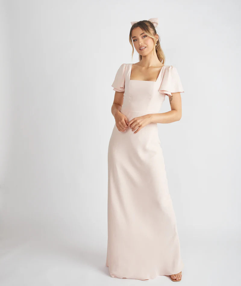 Lady wearing light blush pink crepe bridesmaid dress with square neckline by six stories against a white backdrop