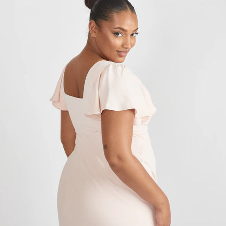 Lady wearing light blush pink crepe bridesmaid dress with square neckline by six stories against a white backdrop