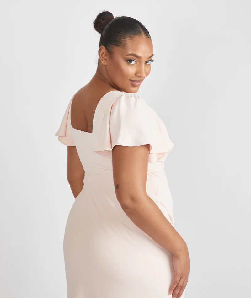 Lady wearing light blush pink crepe bridesmaid dress with square neckline by six stories against a white backdrop