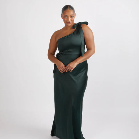 Woman wearing a dark green one-shoulder dress with a bow detail on a white background