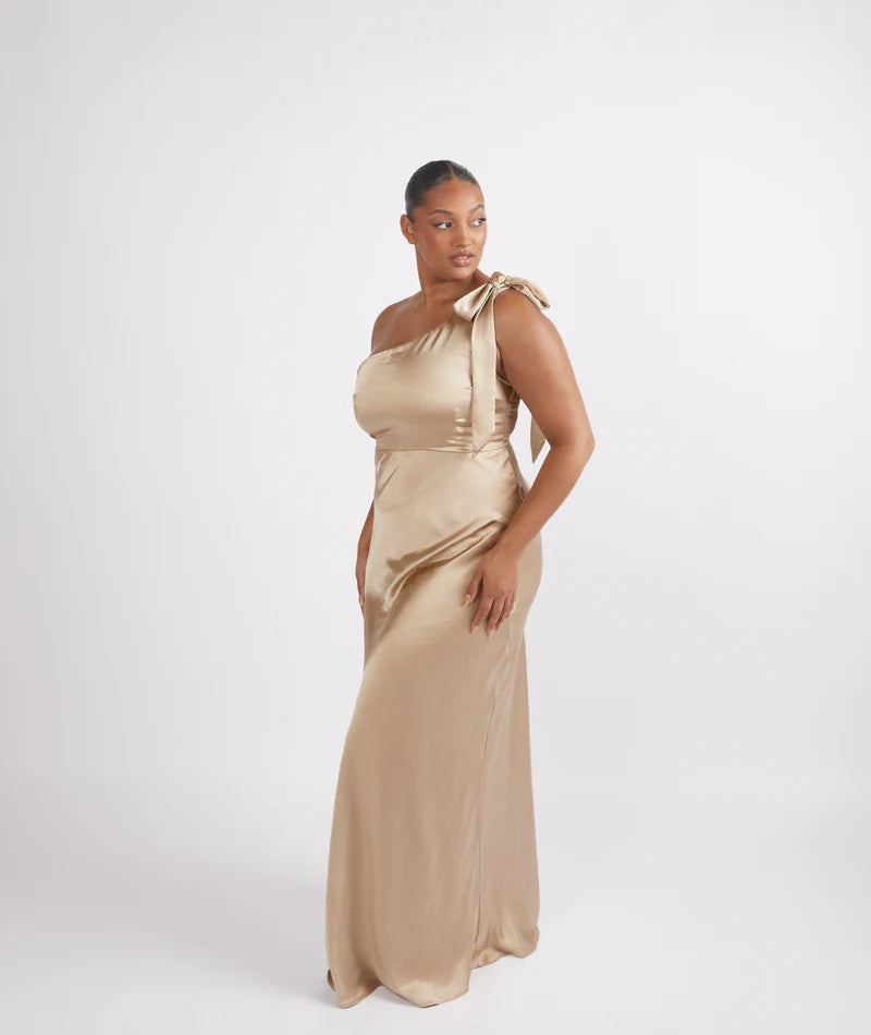 Woman wearing a champagne satin one-shoulder bridesmaid dress on a white background