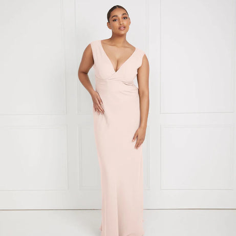 Woman wearing a light pink dress bridesmaid dress by six stories with a V-neckline against a white background