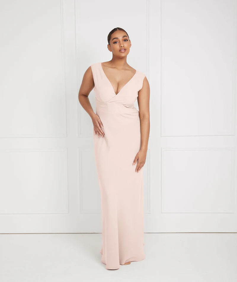 Woman wearing a light pink dress bridesmaid dress by six stories with a V-neckline against a white background