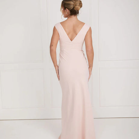 Woman wearing a light pink dress bridesmaid dress by six stories with a V-neckline against a white background