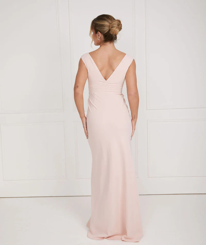 Woman wearing a light pink dress bridesmaid dress by six stories with a V-neckline against a white background