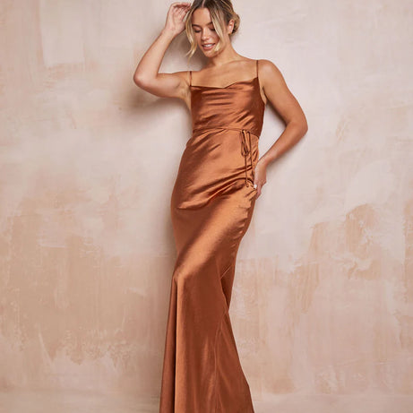 woman wearing long satin rust teracotta gown against a neutral backdrop