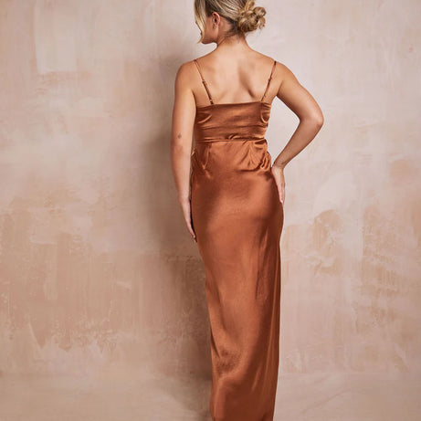 woman wearing long satin rust teracotta gown against a neutral backdrop