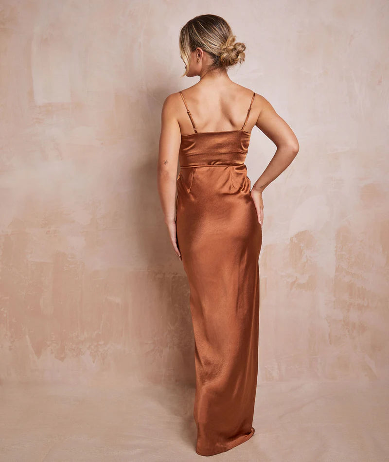 woman wearing long satin rust teracotta gown against a neutral backdrop