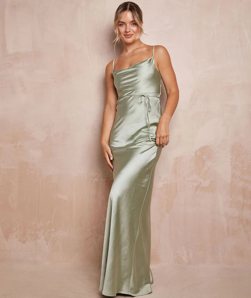 Woman wearing a long green satin dress against a beige background
