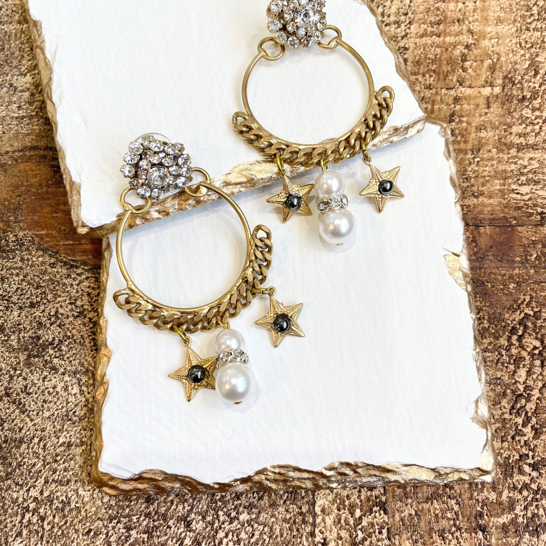 A pair of earrings featuring a gold-colored antique chain circlet with a Swarovski crystal cluster at the top, adorned with pearl, crystal, and starlet charms.