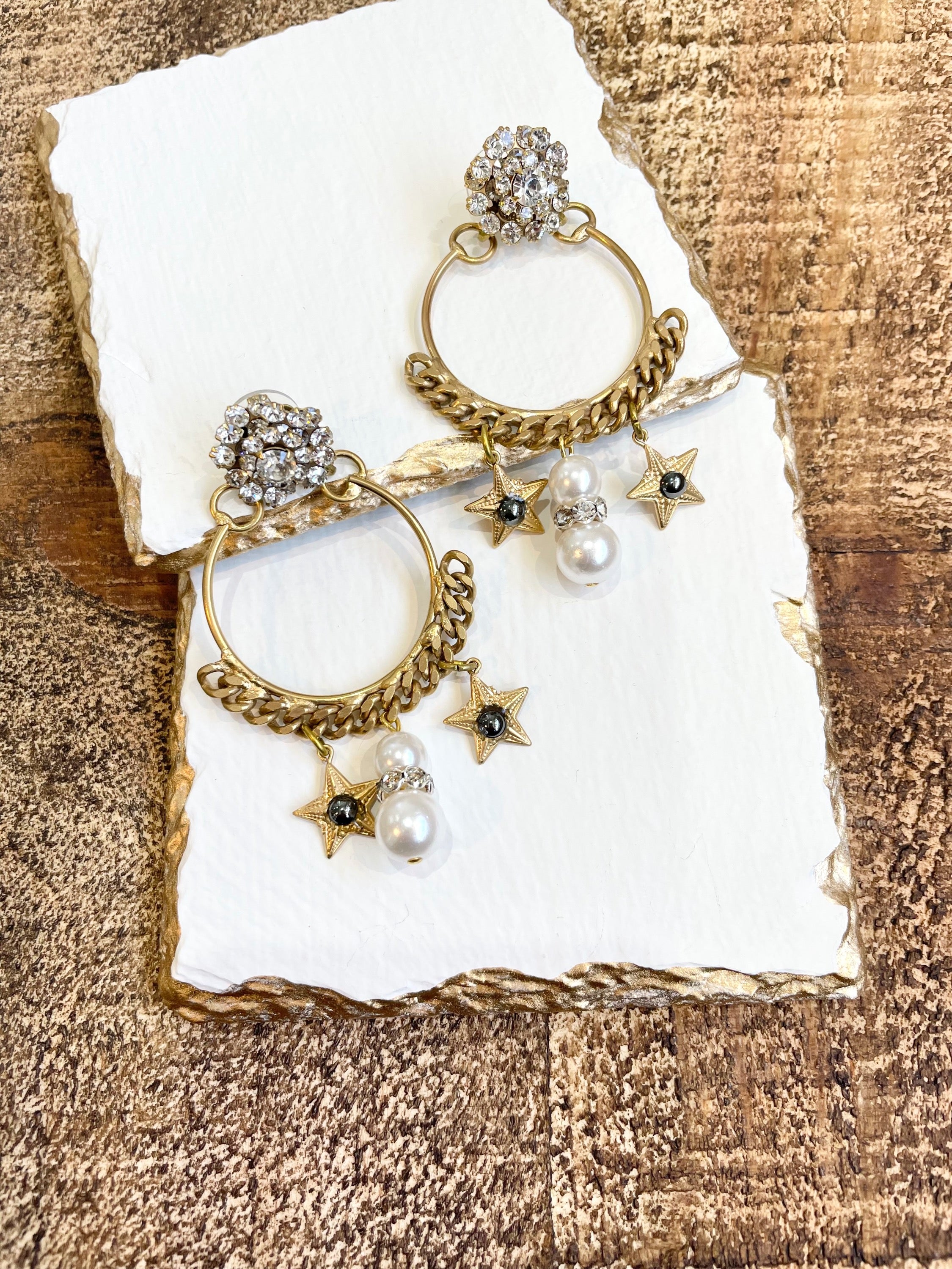 A pair of earrings featuring a gold-colored antique chain circlet with a Swarovski crystal cluster at the top, adorned with pearl, crystal, and starlet charms.