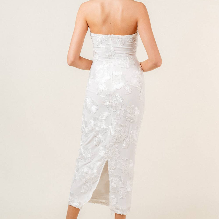 Woman wearing a strapless white floral midi dress on a plain background