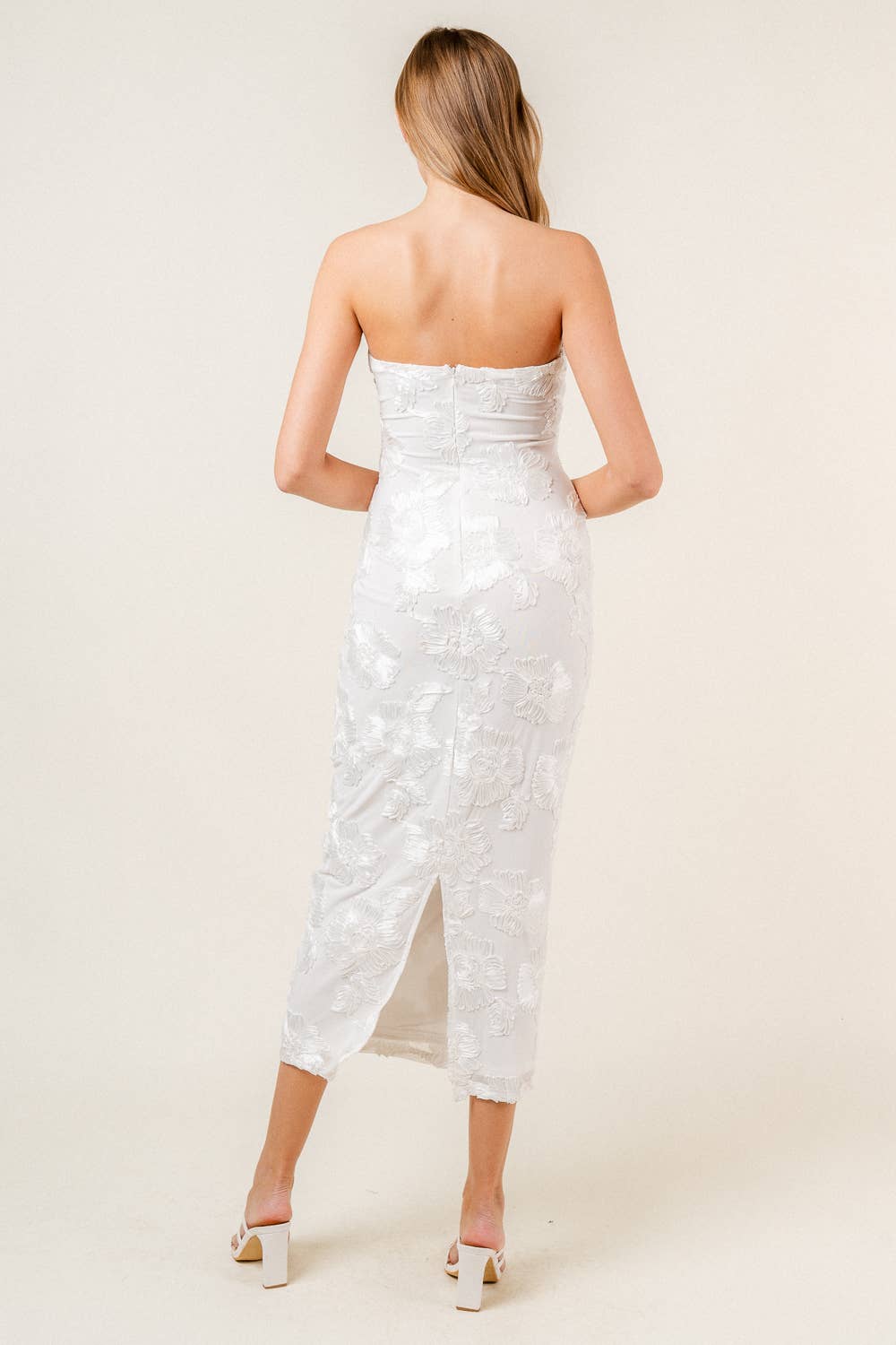 Woman wearing a strapless white floral midi dress on a plain background