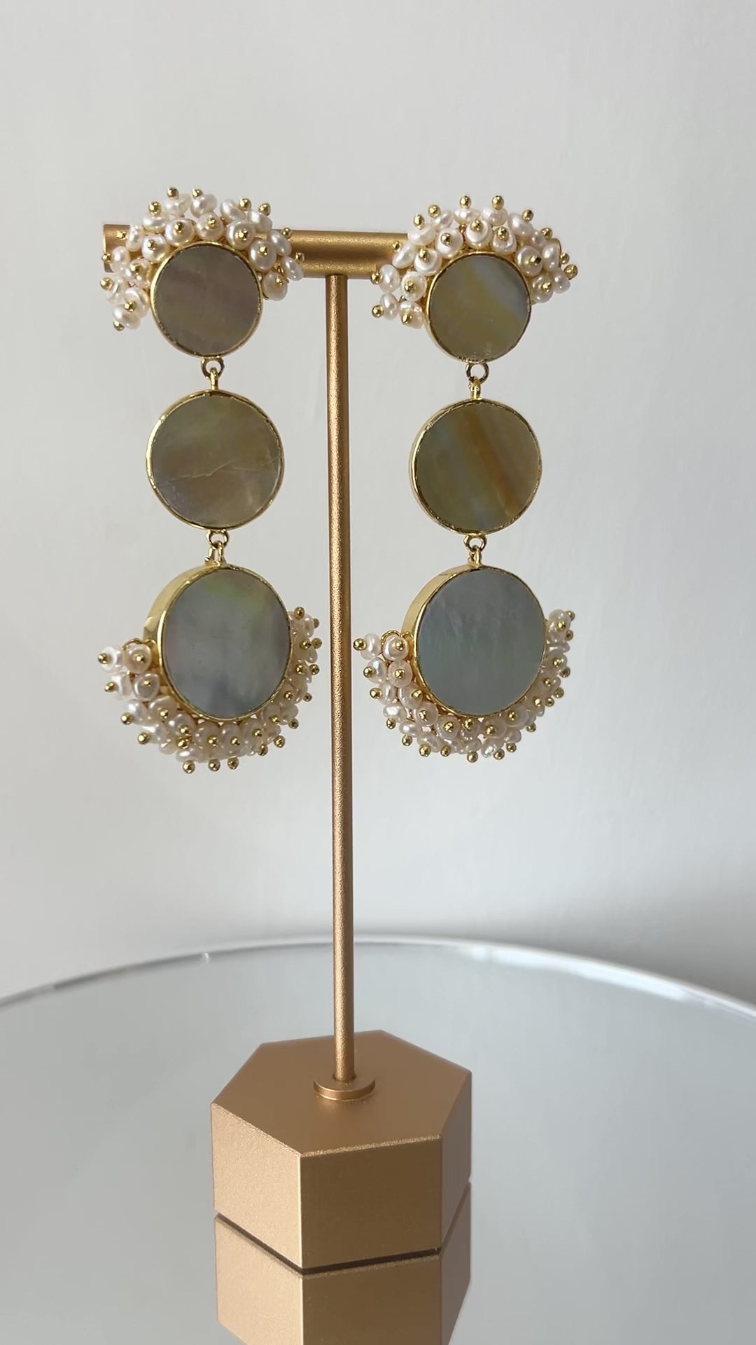 Video of a Pair of statement mother of pearl earrings on a gold stand against a light grey background