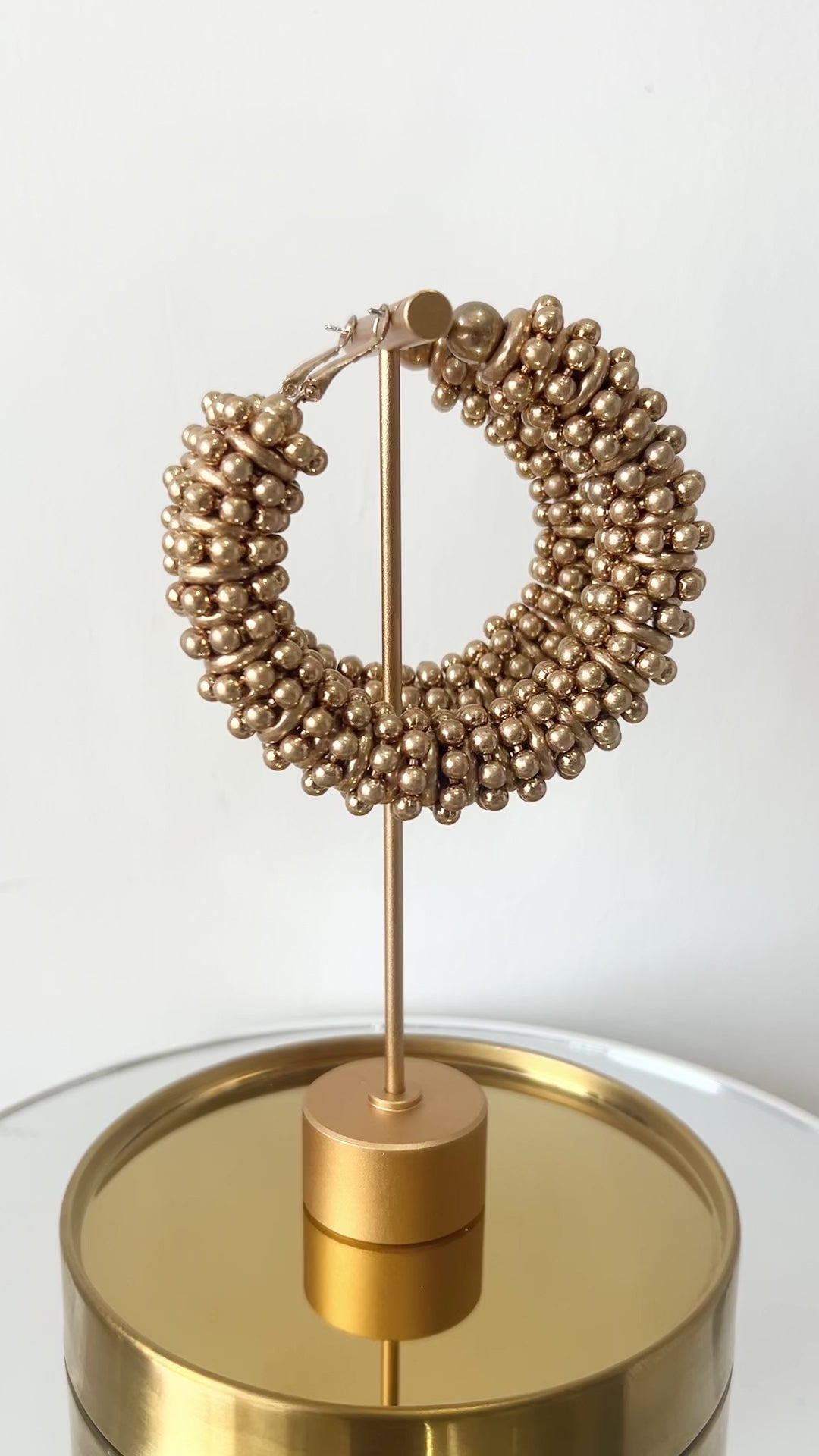 Gold hoop earrings on a stand with a plain background