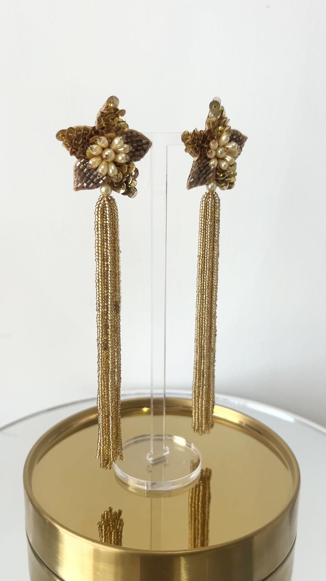 Video of long star shaped gold beaded tassel earrings against a white backdrop.
